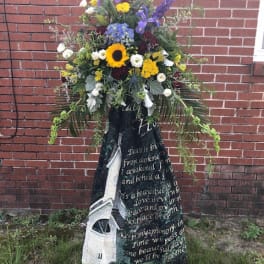 Standing funeral spray with mixed flowers and a memorial blanket drape