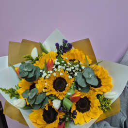 Bouquet of sunflowers, tulips, and white filler flowers wrapped in paper