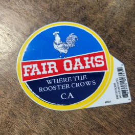 Fair Oaks sticker with a rooster logo on a wood surface