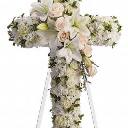 White floral cross on a stand with lilies and roses