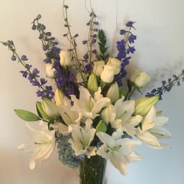 White lilies and purple delphinium in a glass vase