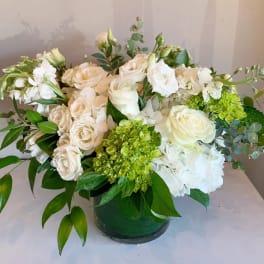 White and cream floral arrangement in a green vase with green accents