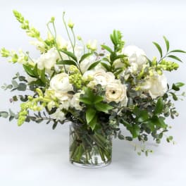 White floral arrangement in a clear glass vase with green foliage