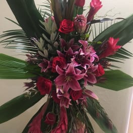 Tall arrangement of red roses and pink lilies with large tropical leaves
