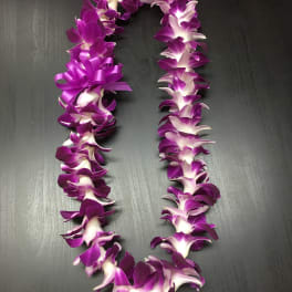 Purple and white orchid lei on a dark surface