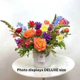 Bright mixed flower arrangement with orange roses, tulips, daffodils and other blooms in a white vase