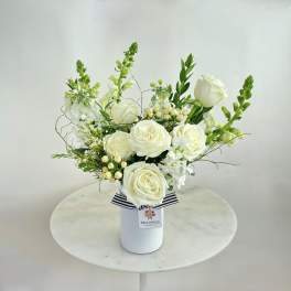 White roses and white blooms arranged in a white vase with a striped ribbon