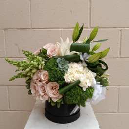 Bouquet of pale pink roses, white lilies, and hydrangeas in a black hatbox