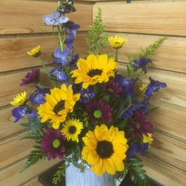 Bouquet of yellow sunflowers and purple daisies in a white vase