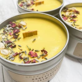 Round yellow wax candles in silver tins topped with dried flower petals and herbs.