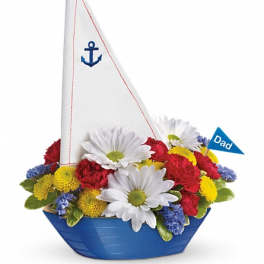 Sailboat-shaped flower arrangement with daisies and carnations in a blue container