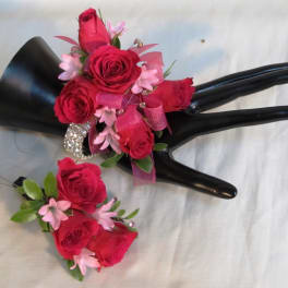 Pink rose corsage and boutonniere with ribbon on a black display hand