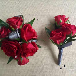 Two red rose boutonnieres with ribbon and rhinestone accents