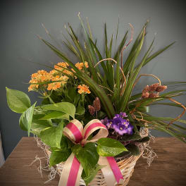 Basket arrangement with orange and purple flowers and a pink ribbon