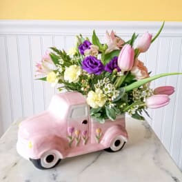 Pink tulips and mixed flowers arranged in a pink ceramic truck planter