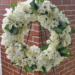 White floral wreath on a black stand against a brick wall