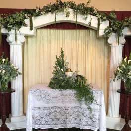 Floral altar display with white flowers and greenery on columns and a table