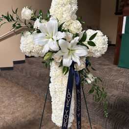 White floral cross on a stand with ribbon streamers
