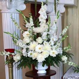Large all-white arrangement of roses, daisies, and mums in a white pedestal vase