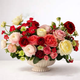 Mixed pink, red, and cream flowers arranged in a cream pedestal vase
