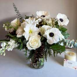 White floral arrangement in a glass vase with a candle beside it