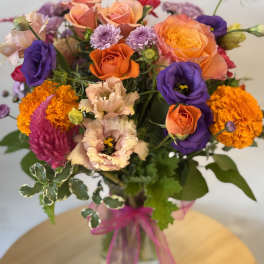 Mixed bouquet of orange, purple, and pink flowers in a glass vase
