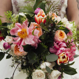 A bride holds a bouquet of pink, peach, and white flowers.