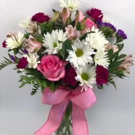 Bouquet of pink roses, white daisies, and mixed blooms in a glass vase with a pink ribbon