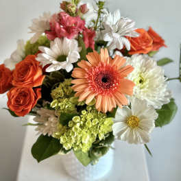 Mixed bouquet of orange roses, daisies, and pink blooms in a white vase