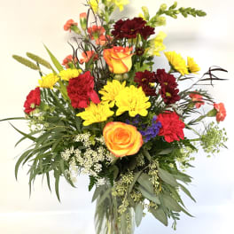 Mixed bouquet of roses, carnations, and yellow blooms in a glass vase