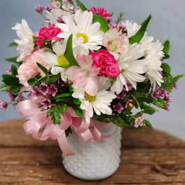 White daisies and pink blooms in a white textured vase with a pink ribbon bow.