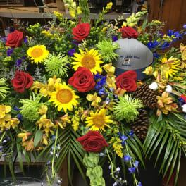 Large floral arrangement with red roses, sunflowers, and a gray baseball cap
