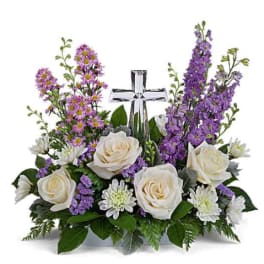 White roses and purple flowers arranged around a clear glass cross