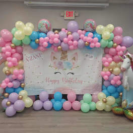Pastel balloon arch with unicorn birthday backdrop and foil unicorn balloons