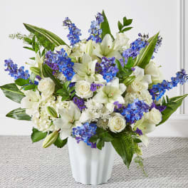 White lilies and roses with blue flowers in a white vase