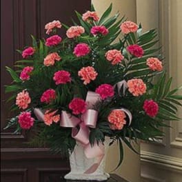 Pink and coral carnations in a white vase with a pink ribbon