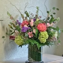 Tall mixed arrangement of pink, green, and purple flowers in a clear glass cylinder vase