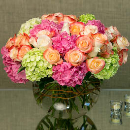 Low round arrangement of peach roses and pink and green hydrangeas in a clear glass bowl vase