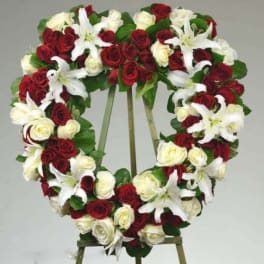 Heart-shaped wreath of red and white roses with white lilies on an easel