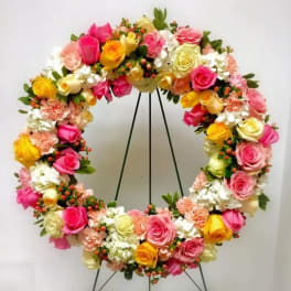 Circular floral wreath with pink, yellow, and white roses on a stand