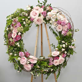 Circular floral wreath with pink and white roses on a wooden stand