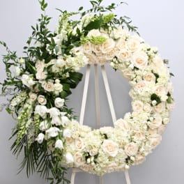 Large white floral wreath on an easel with cream roses and greenery