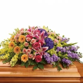 Colorful floral casket spray with pink lilies, roses, and purple blooms