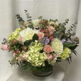 Pastel arrangement of pink roses, white mums, and green hydrangeas in a clear glass vase.