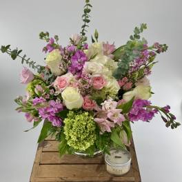 Pink and white mixed flower arrangement in a glass vase with a green bloom and a small candle beside it