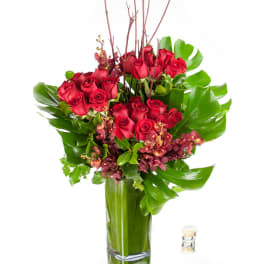 Tall arrangement of red roses and burgundy orchids with large tropical leaves in a glass vase