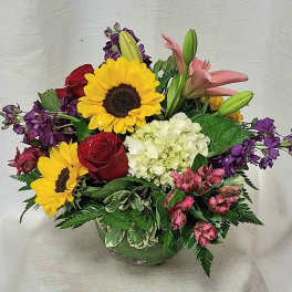 Mixed arrangement of sunflowers, roses, lilies, and hydrangea in a clear glass vase