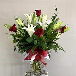 Tall arrangement of red roses and white lilies in a clear vase with a red bow.