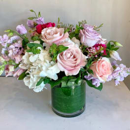 Pink and lavender roses arranged with white hydrangeas in a green glass vase.