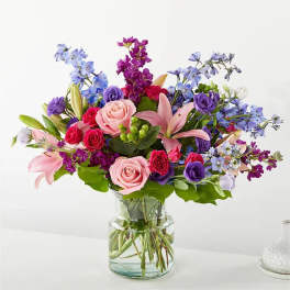 Mixed bouquet of pink roses, lilies, and purple flowers in a glass vase